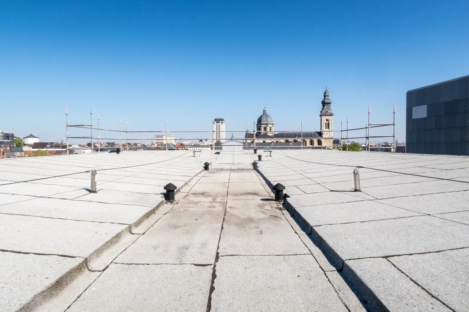 Rooftop with tiled walkway and distant church towers under a clear blue sky