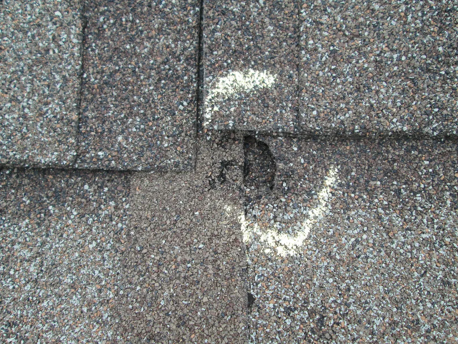 Close-up of a gray shingle roof with a damaged spot and white patching around it