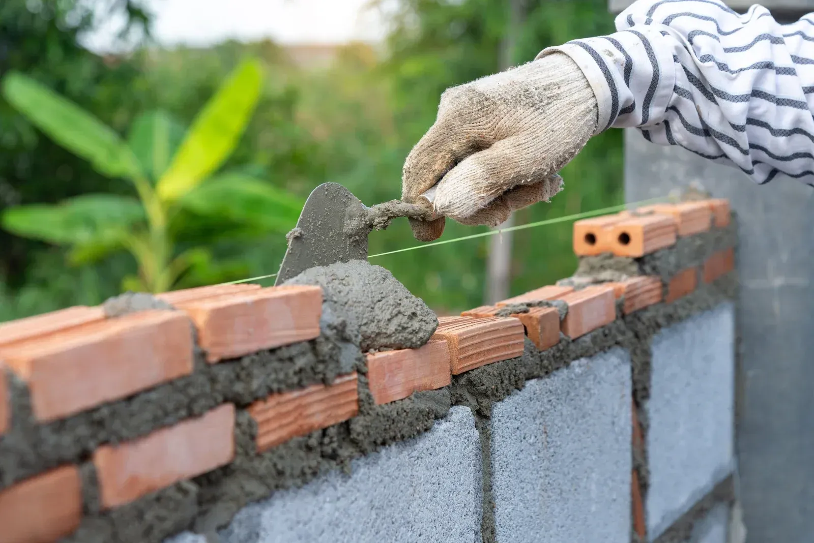 Gloved hand spreading wet mortar on a brick wall under construction