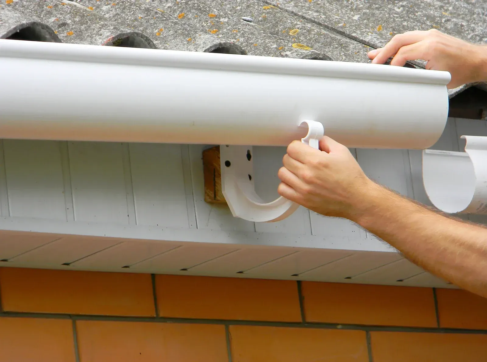 Hands installing a white rain gutter on a house roofline