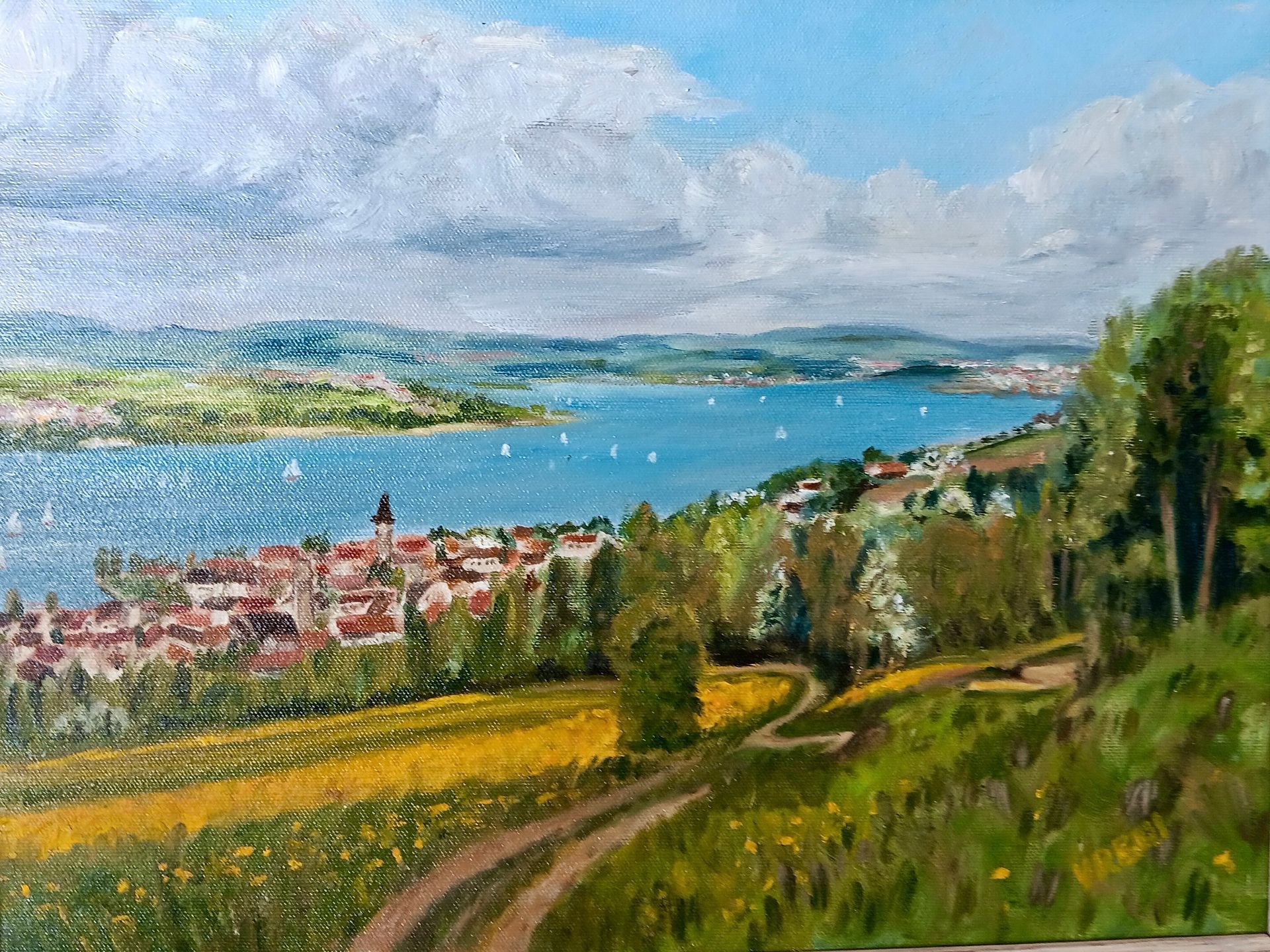 Scenic oil painting: lakeside village with red roofs, winding road through yellow field, blue water, white clouds.