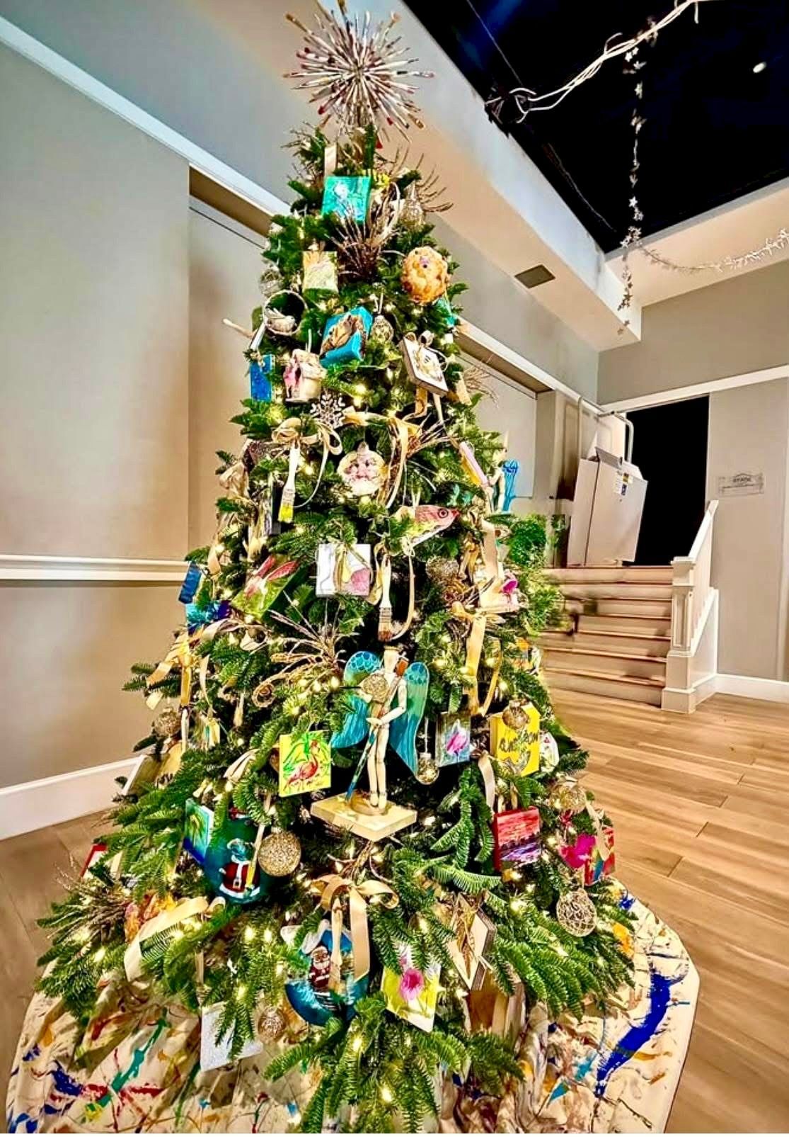 Christmas tree with colorful ornaments and gifts in a hallway with stairs.