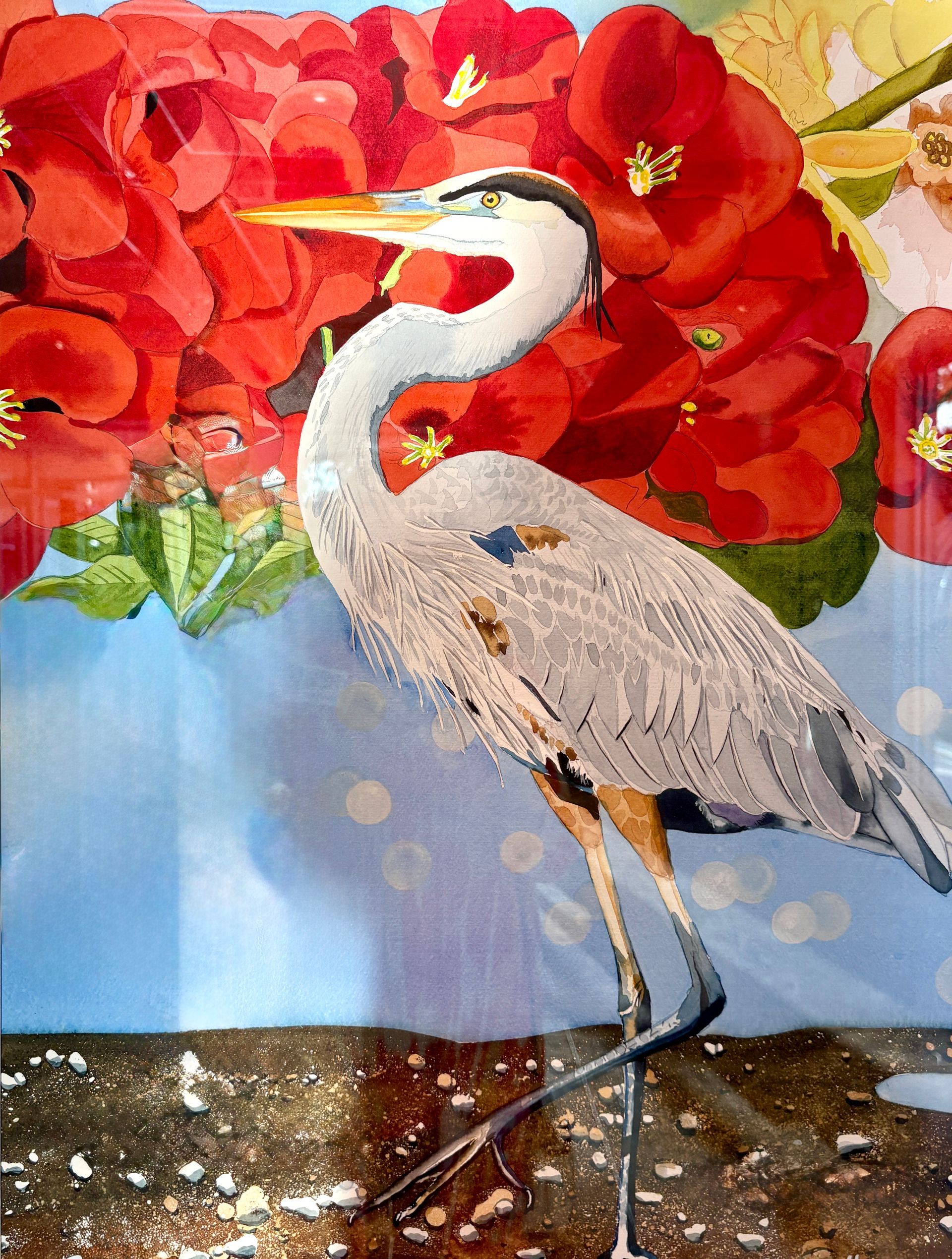 A great blue heron stands before red flowers against a blue background.