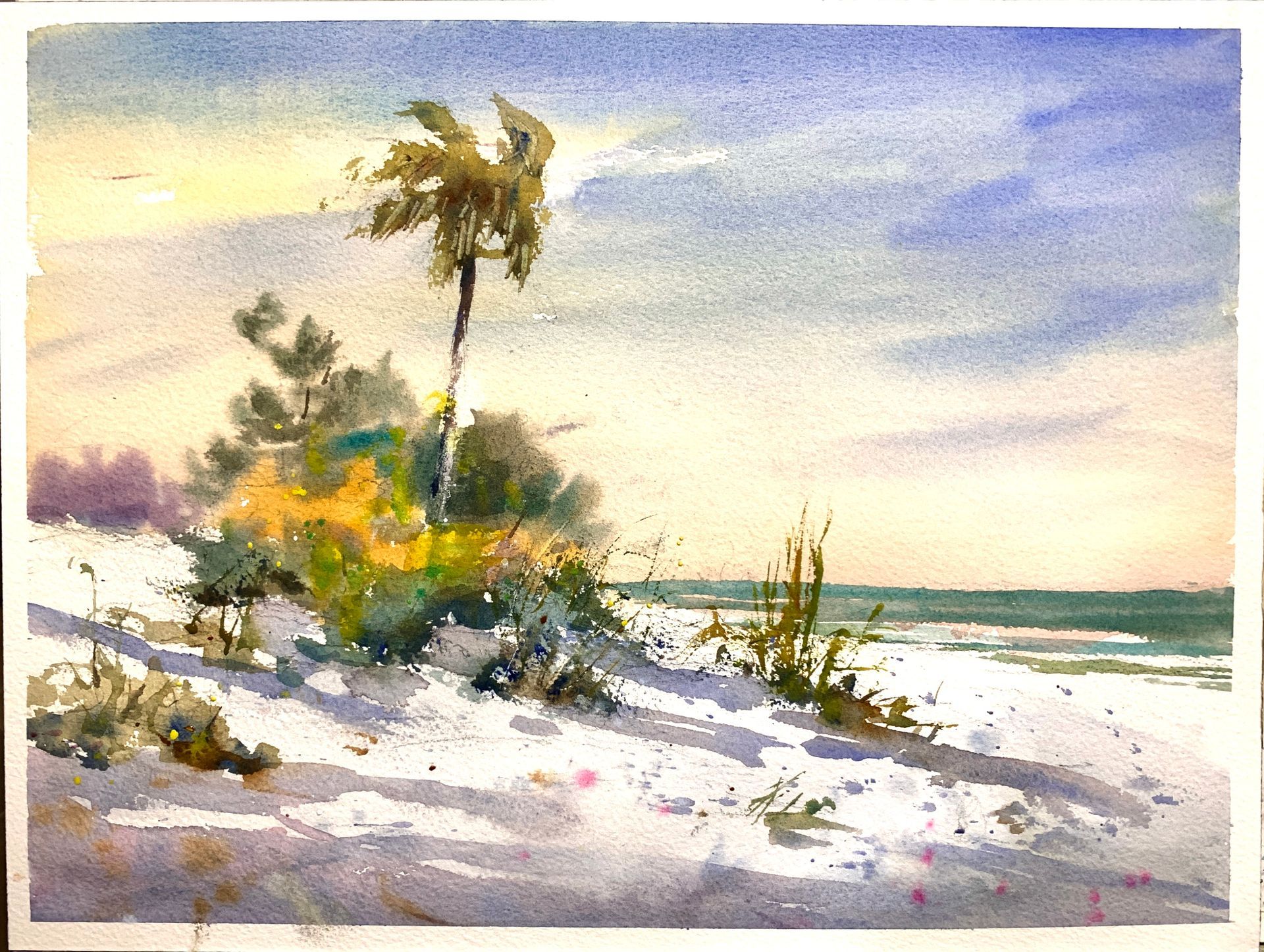 Watercolor painting of a sandy beach with palm tree and vegetation, blue sky, and ocean.