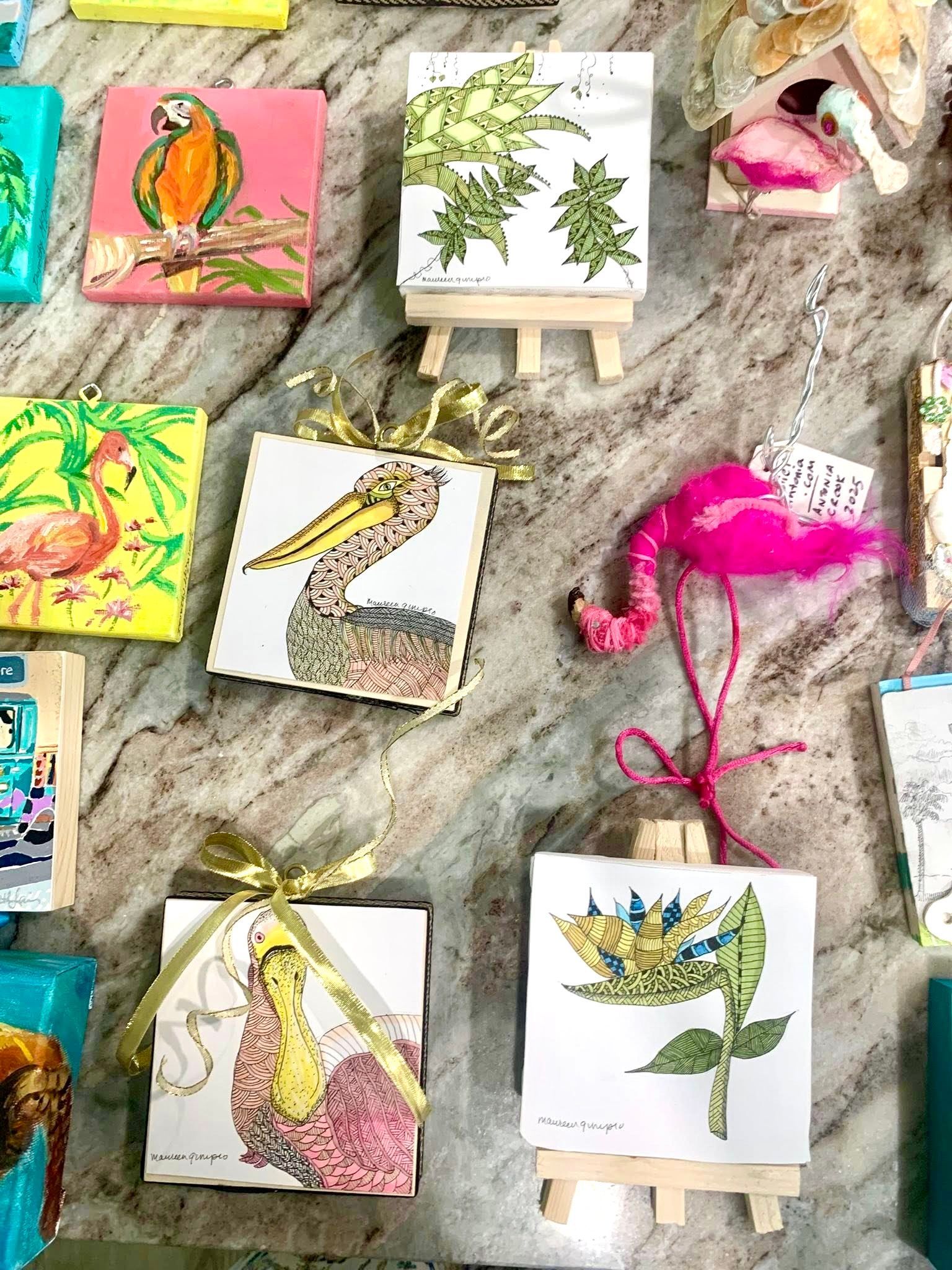 Array of small, square paintings featuring birds, plants, and a flamingo on easels, in vibrant colors.