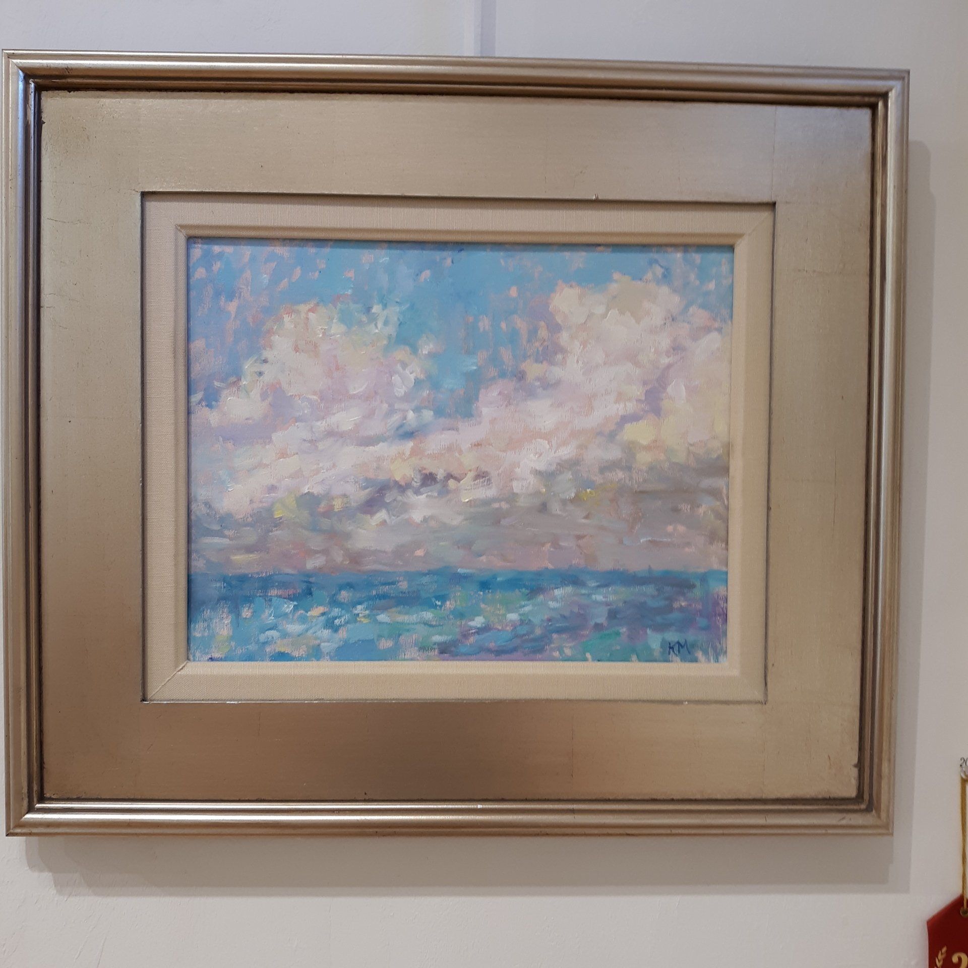 Painting of sea and sky with large white and pink clouds, blue water, framed in gold.