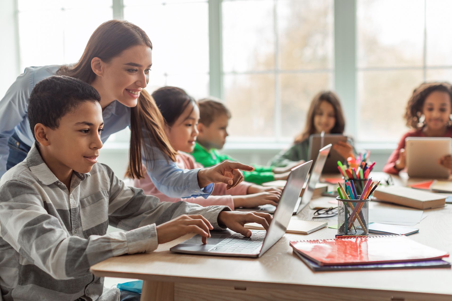 Kids' classroom with teacher helping student on laptop