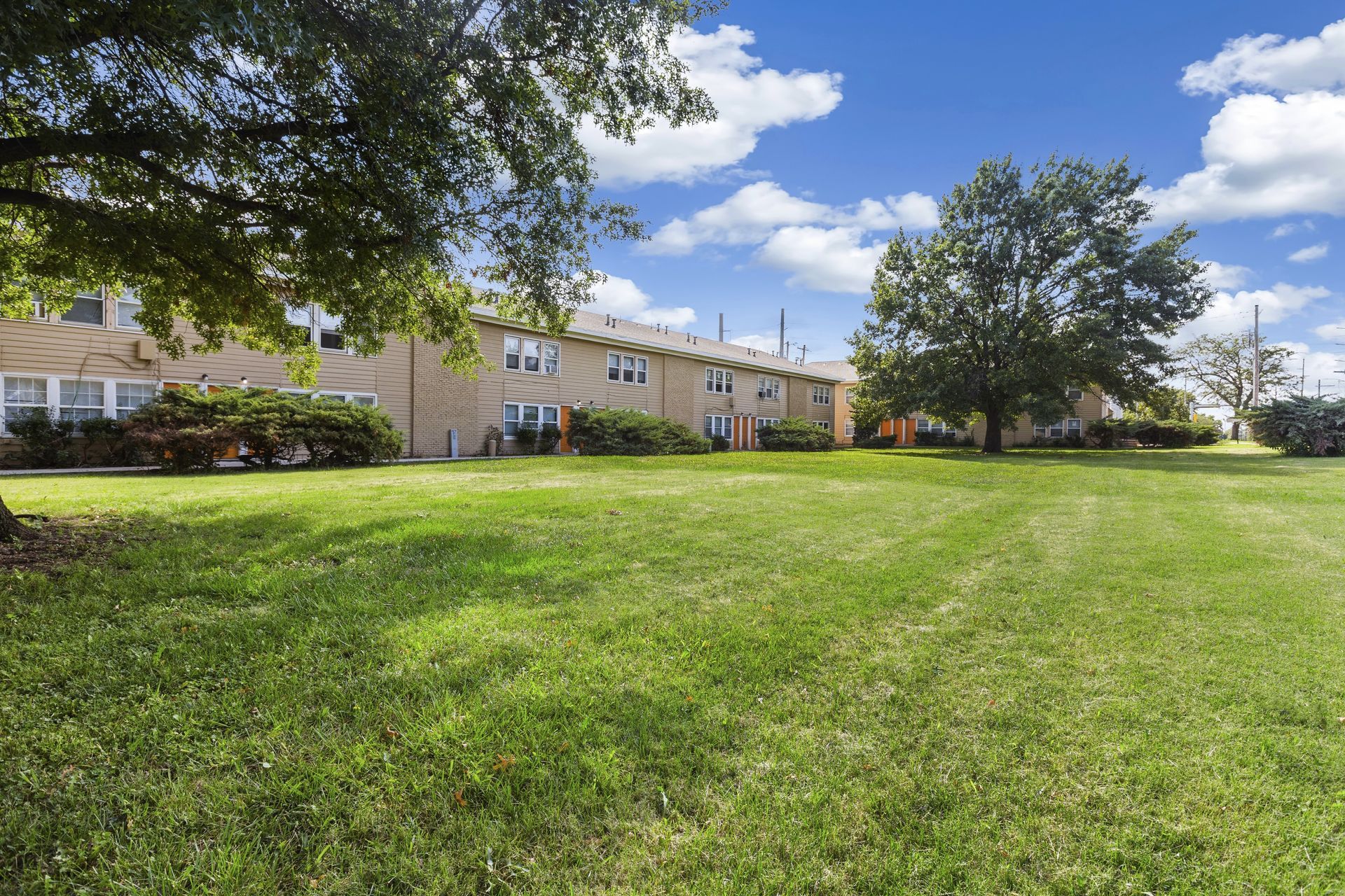 Lawn with green grass in front of a row of apartment buildings. Blue sky with clouds.
