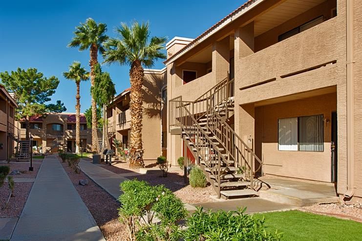 Apartment courtyard with tan buildings, exterior staircases, palm trees, and a sunny walkway