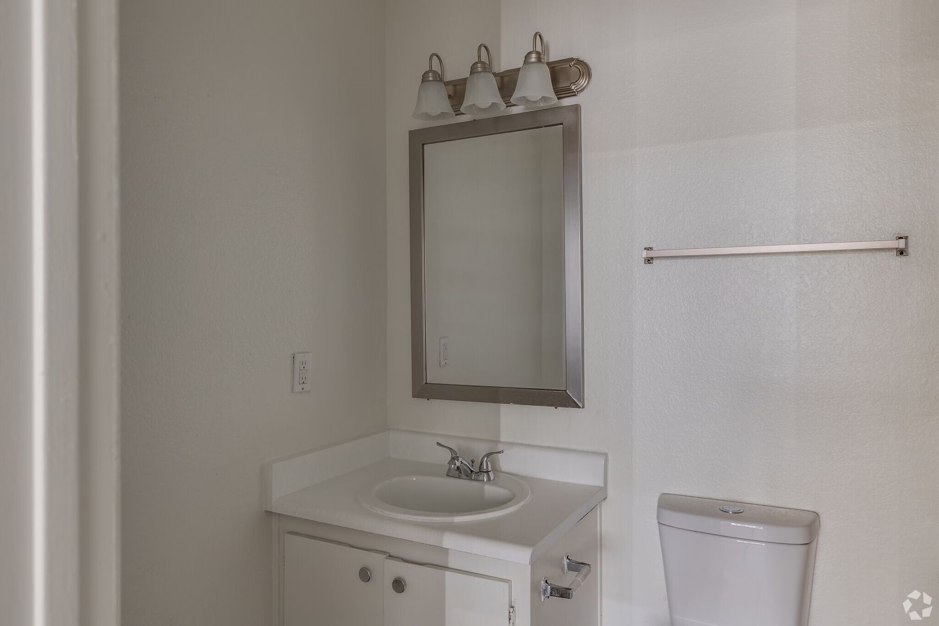 Small bathroom vanity with mirror, light fixture, towel bar, and toilet paper holder.