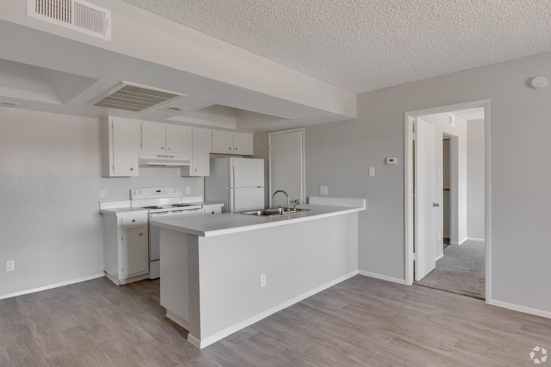 Empty modern kitchen and dining area with white cabinets, gray walls, and wood-look flooring