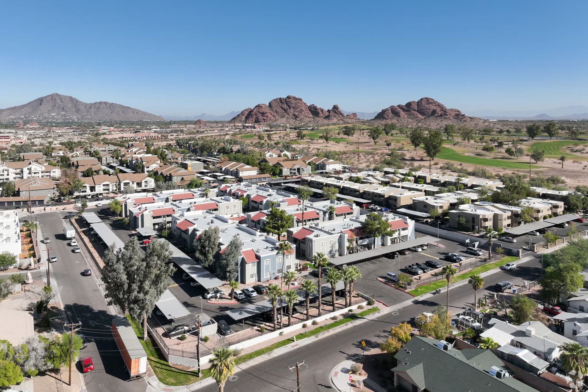 Aerial view of a suburban neighborhood with homes, palm trees, roads, and desert mountains in the background