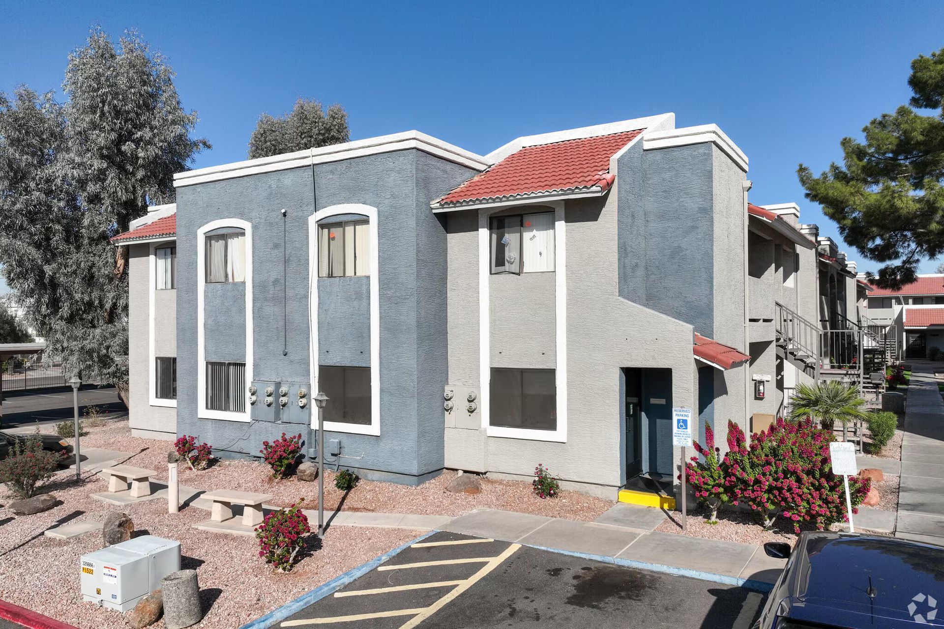 Modern gray apartment building with red roof, balconies, and landscaped front walkway