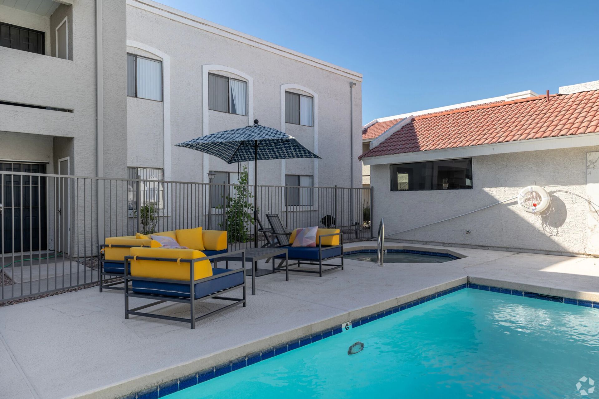 Apartment pool patio with yellow-cushioned seating, umbrella, and turquoise swimming pool