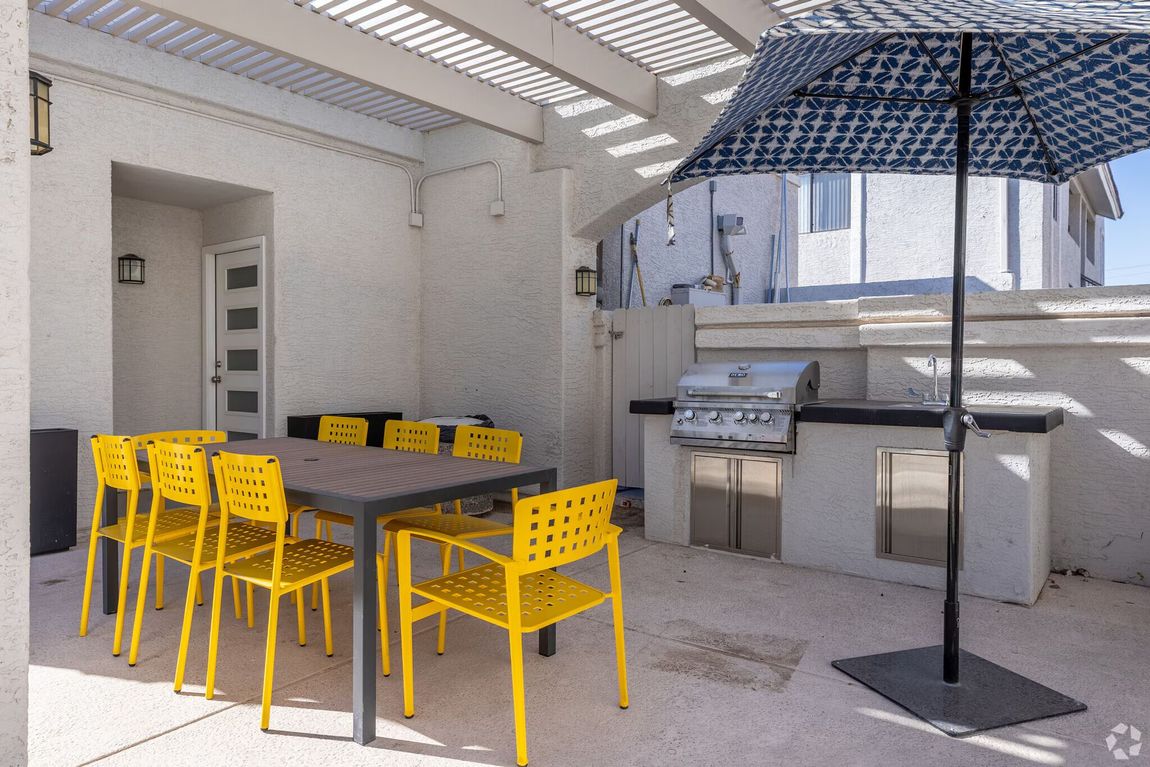 Outdoor patio with yellow chairs, dark table, grill, and a large umbrella in a bright courtyard