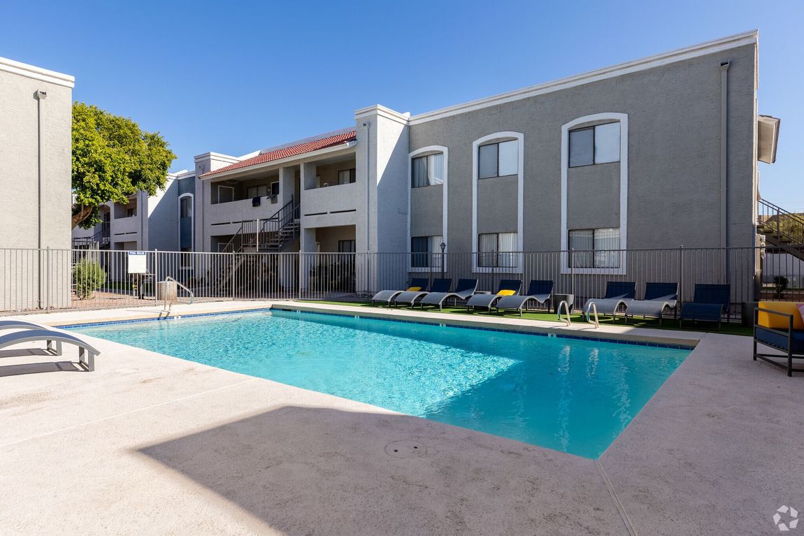 Apartment complex swimming pool with lounge chairs and a white deck under a clear sky