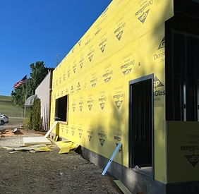 Exterior of a building under construction, covered in yellow sheathing. There is an open door frame and window frame visible.