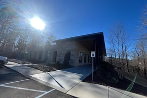 Modern brick building with a sloped roof and long windows on a sunny day. A concrete walkway leads to the entrance.