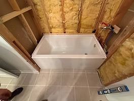 A white bathtub is installed between wooden framing in a bathroom under construction.
