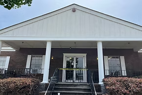 A brick building with white pillars and a peaked roof. Yellow caution tape is strung across the glass doors.