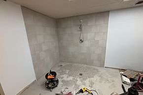 Bathroom under construction with gray tiled shower walls, white drywall, and tools scattered on the floor.