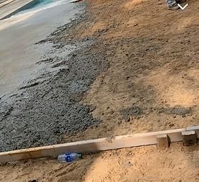 Freshly poured concrete next to compacted soil; a wooden leveler and a water bottle are visible.