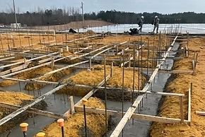 Construction site: Wooden forms and rebar set for foundation, workers in the background, overcast day.