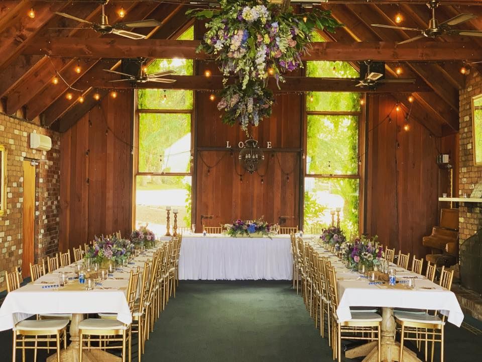Long dining tables in a rustic venue, decorated with flowers, awaiting guests.
