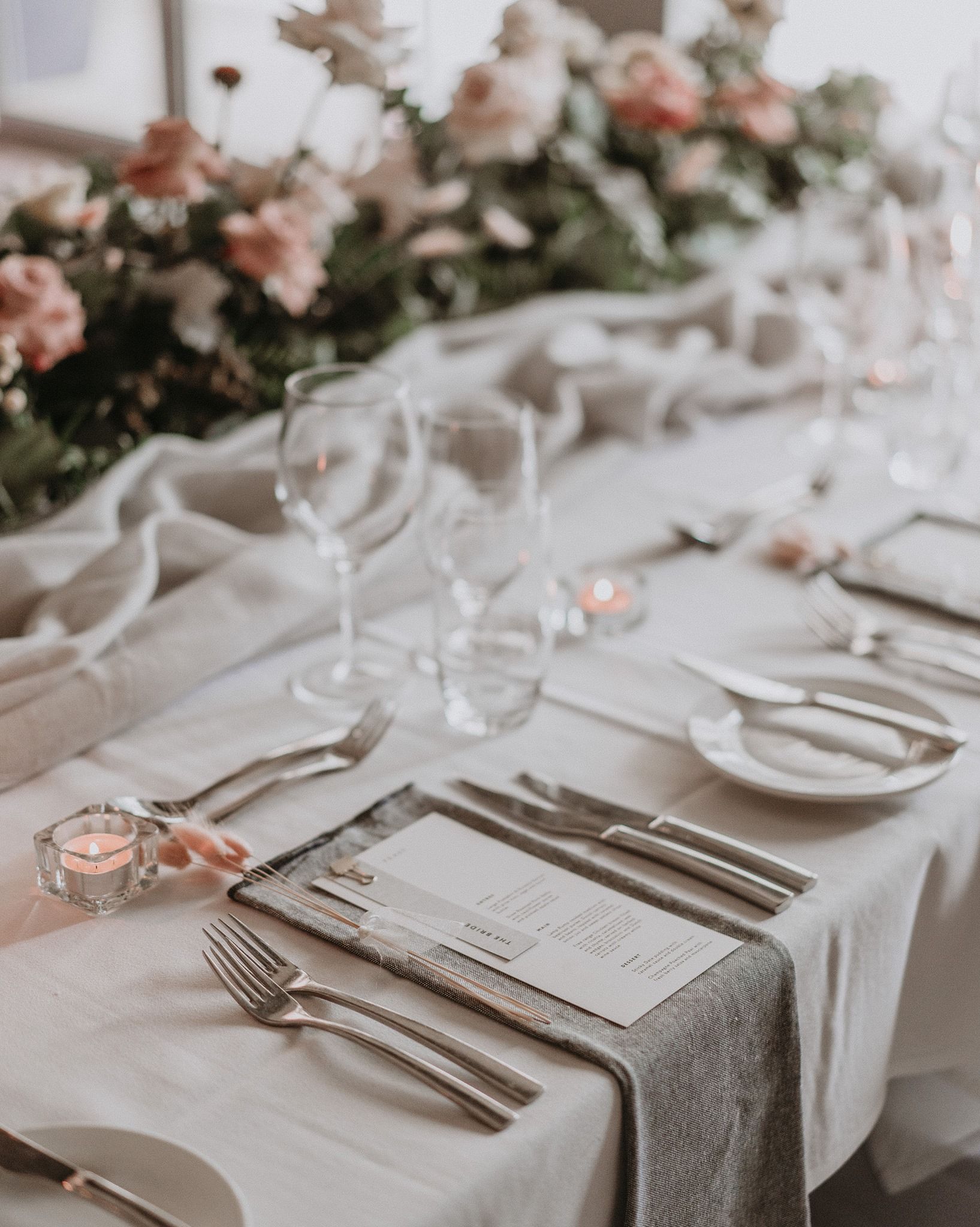 Elegant table setting with floral centerpiece, gray runner, and place settings with glassware and menus.