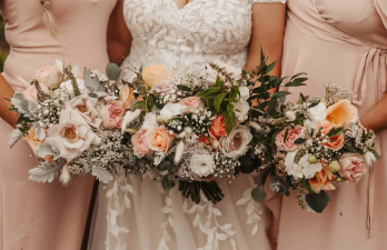 A bride and her bridesmaids are covering their faces with bouquets of flowers.