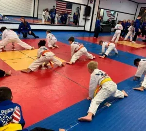Children practicing martial arts drills on red and blue mats in a gymnasium.