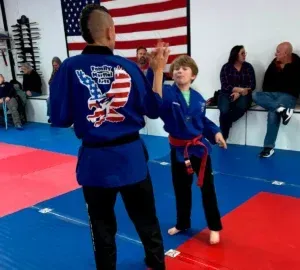 Martial arts class with two people in blue gis practicing a hand technique on red and blue mats