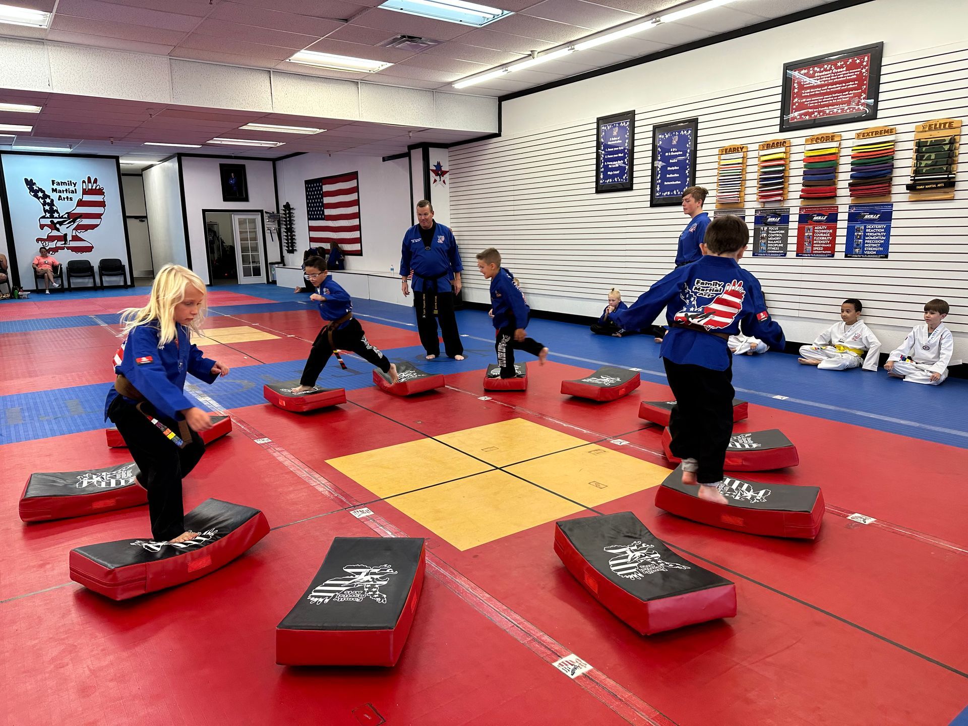 Karate students in white uniforms pose on a red mat, with a child seated front and center holding an orange belt.