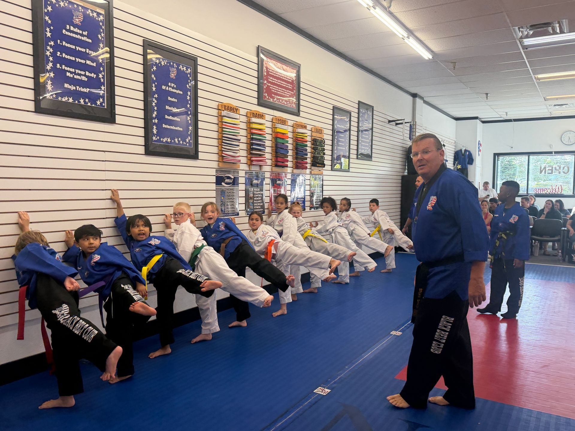 Martial arts class practicing punches in white uniforms with colored belts on blue mats