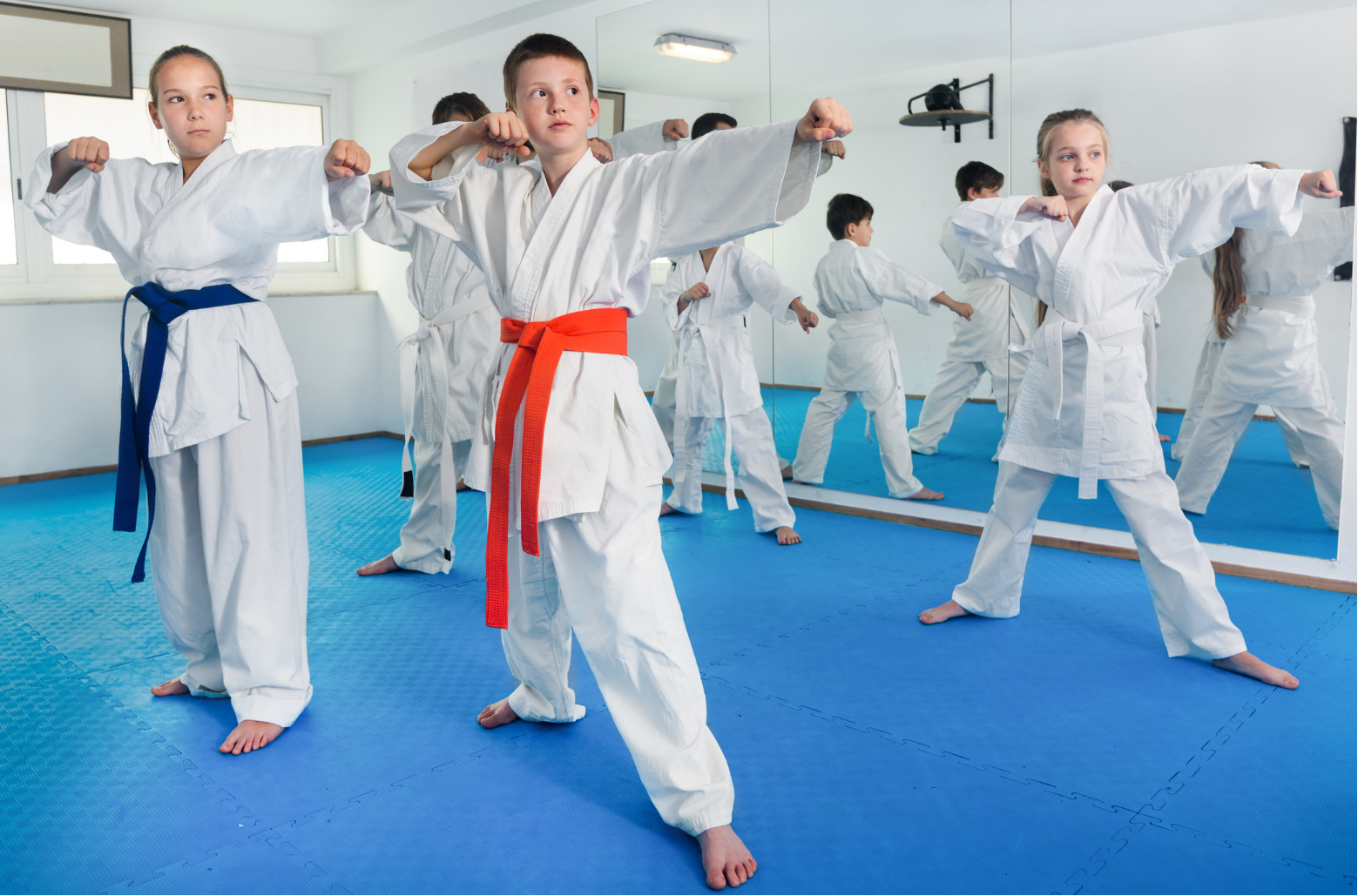 Martial arts class practicing punches in white uniforms with colored belts on blue mats
