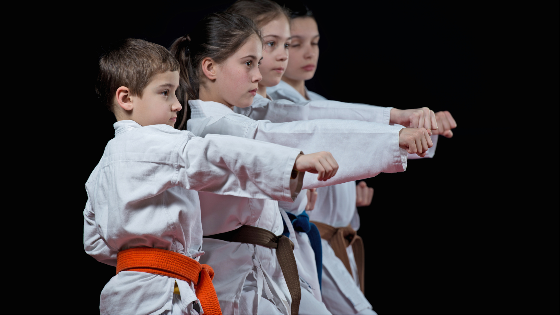 Three karate students in white gis and belts practicing a punch in unison against a black background