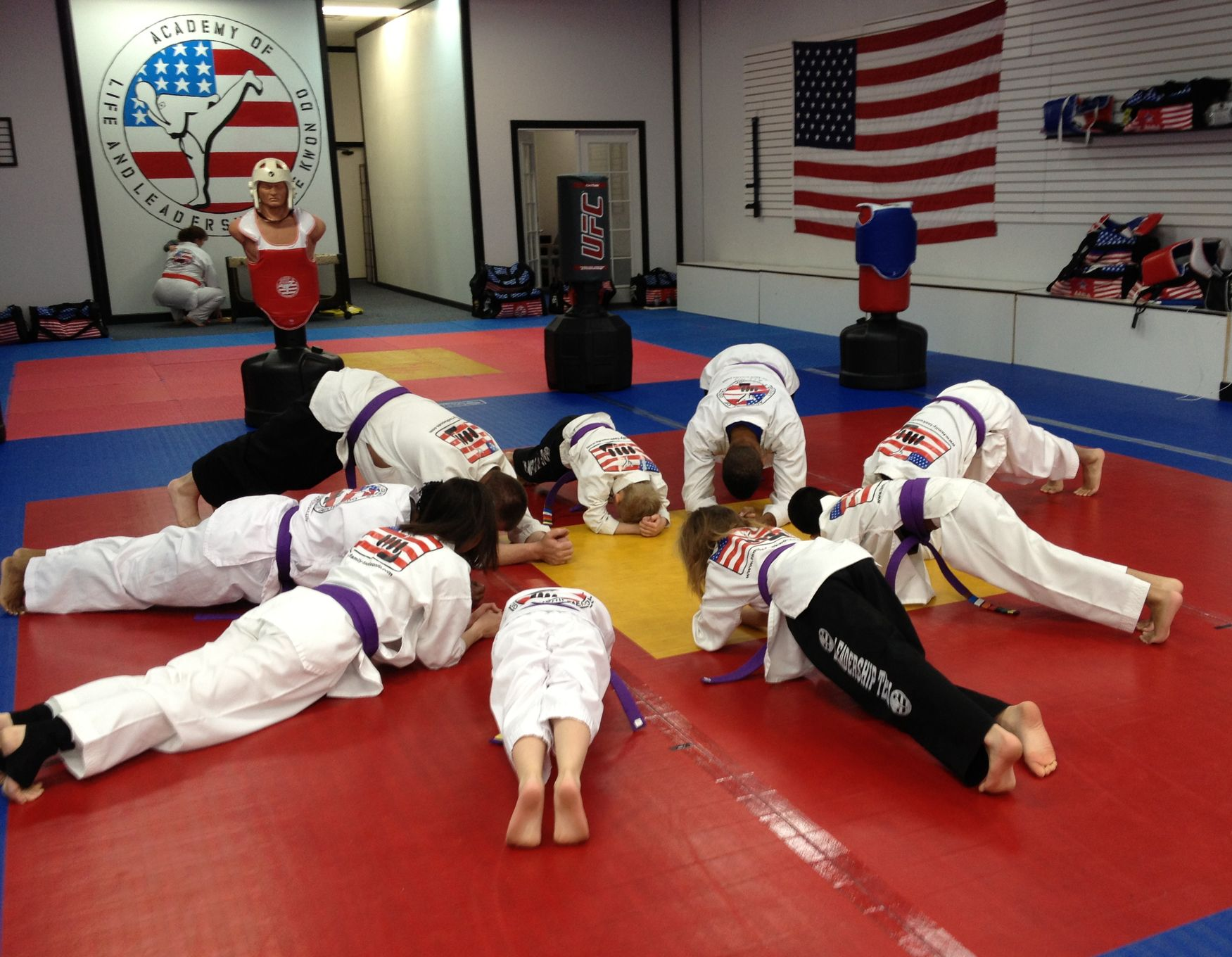 Five children in white karate uniforms standing together, smiling in a bright studio, some with yellow belts