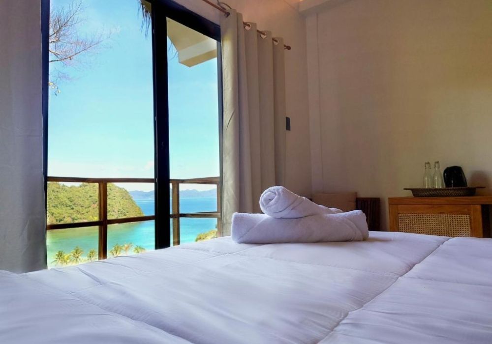 A bed with towels on it in a hotel room with a view of the ocean.