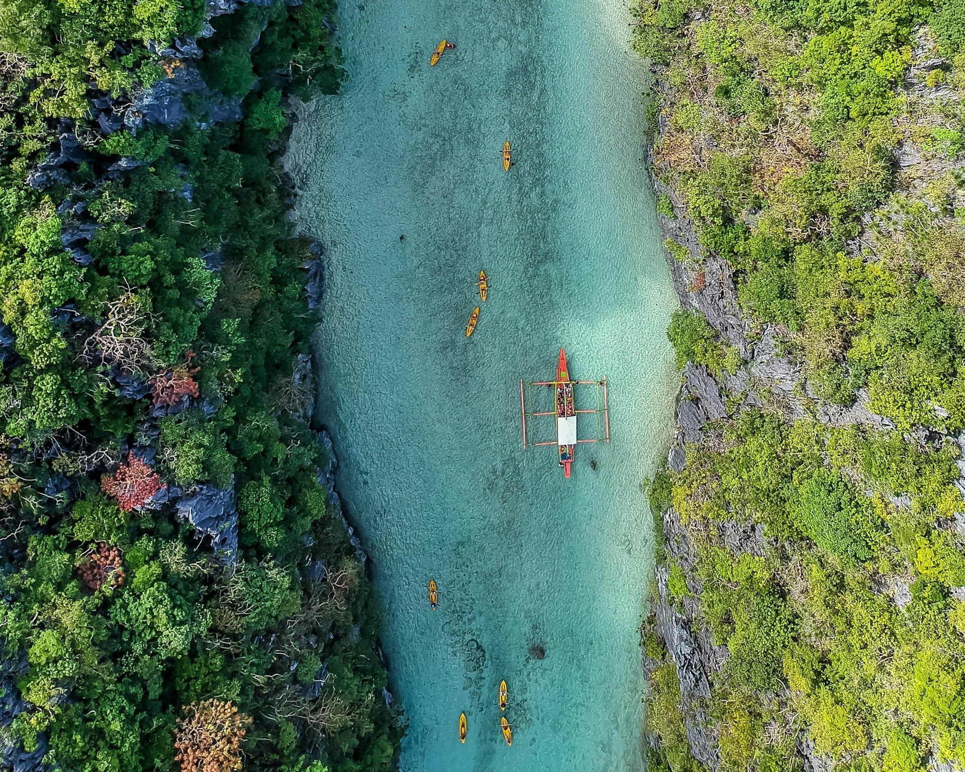 An aerial view of a group of people kayaking down a river surrounded by trees.