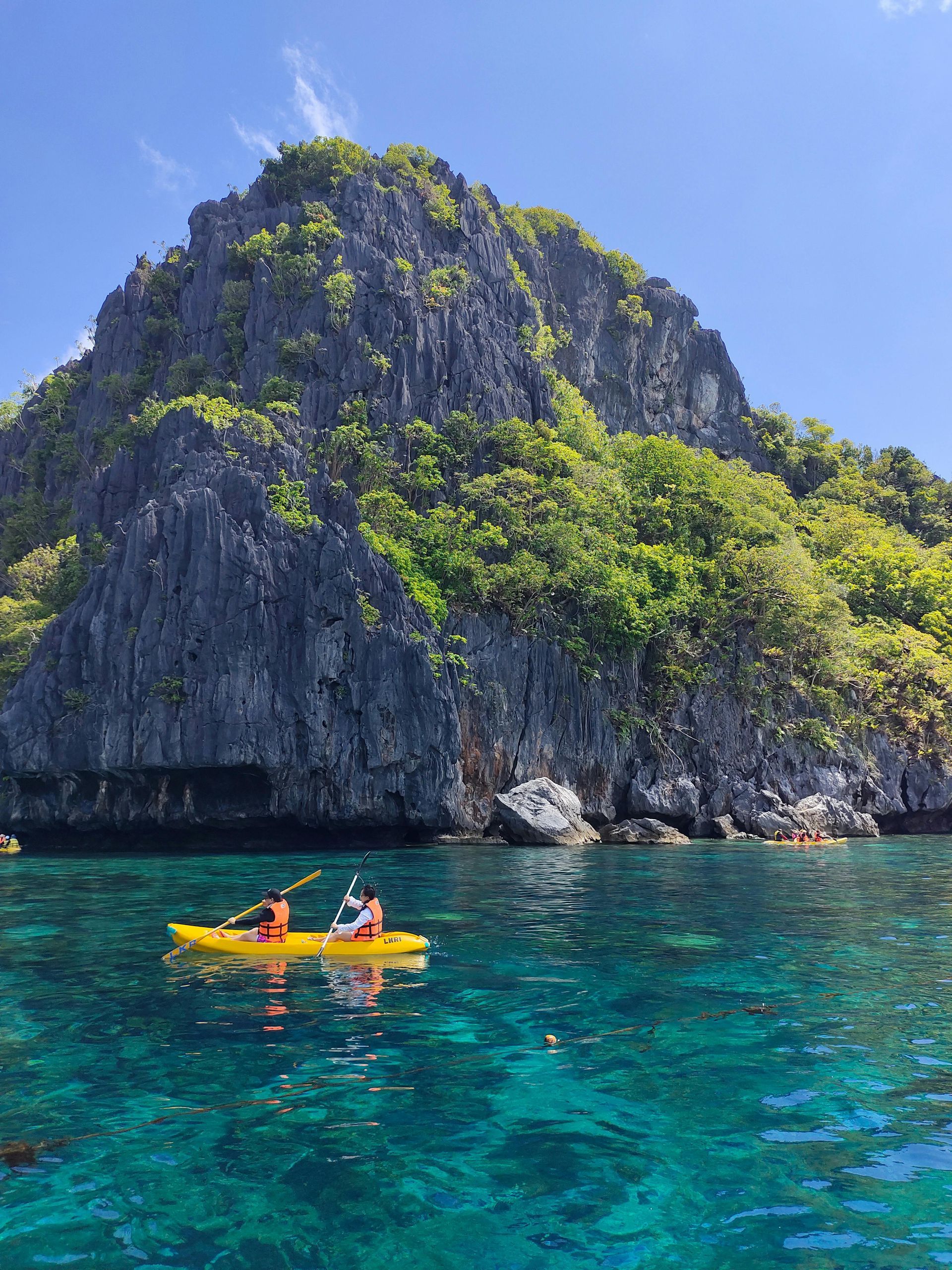 Two people are kayaking in the ocean near a rocky island.