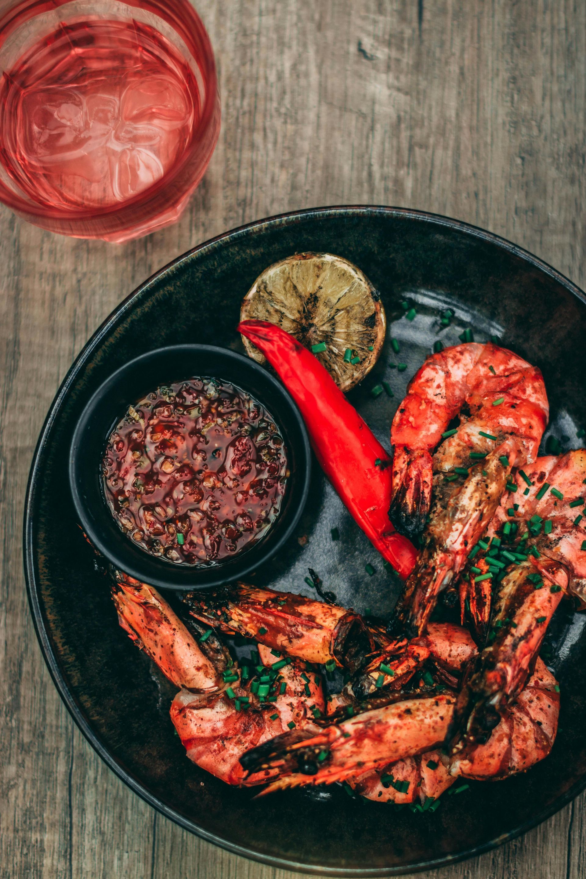 A plate of shrimp with sauce and a glass of water on a wooden table.