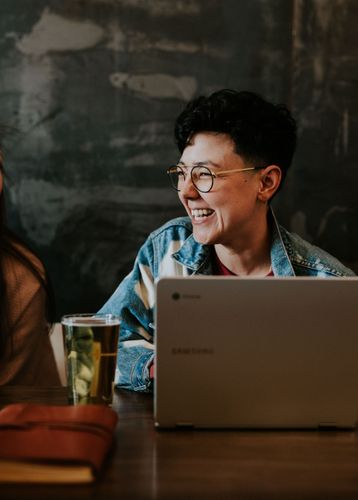 A woman is sitting at a table with a laptop and smiling.