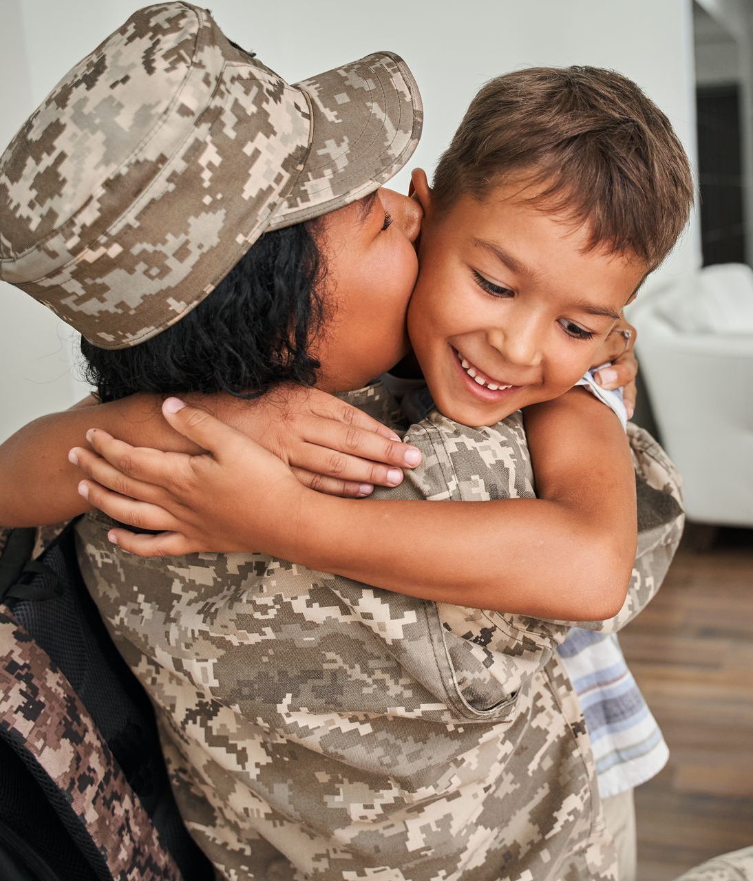 A woman in a military uniform kisses a young boy on the cheek.