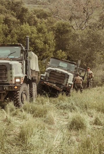 A group of military vehicles are driving through a grassy field.