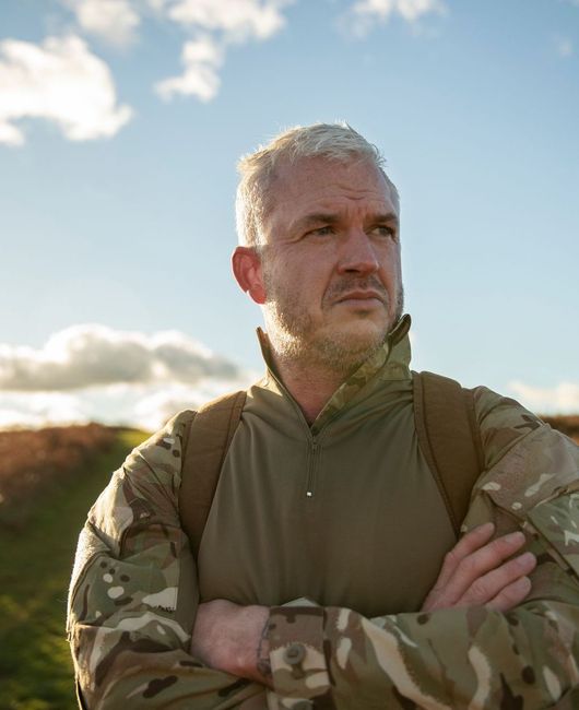 A man in a camouflage jacket with his arms crossed