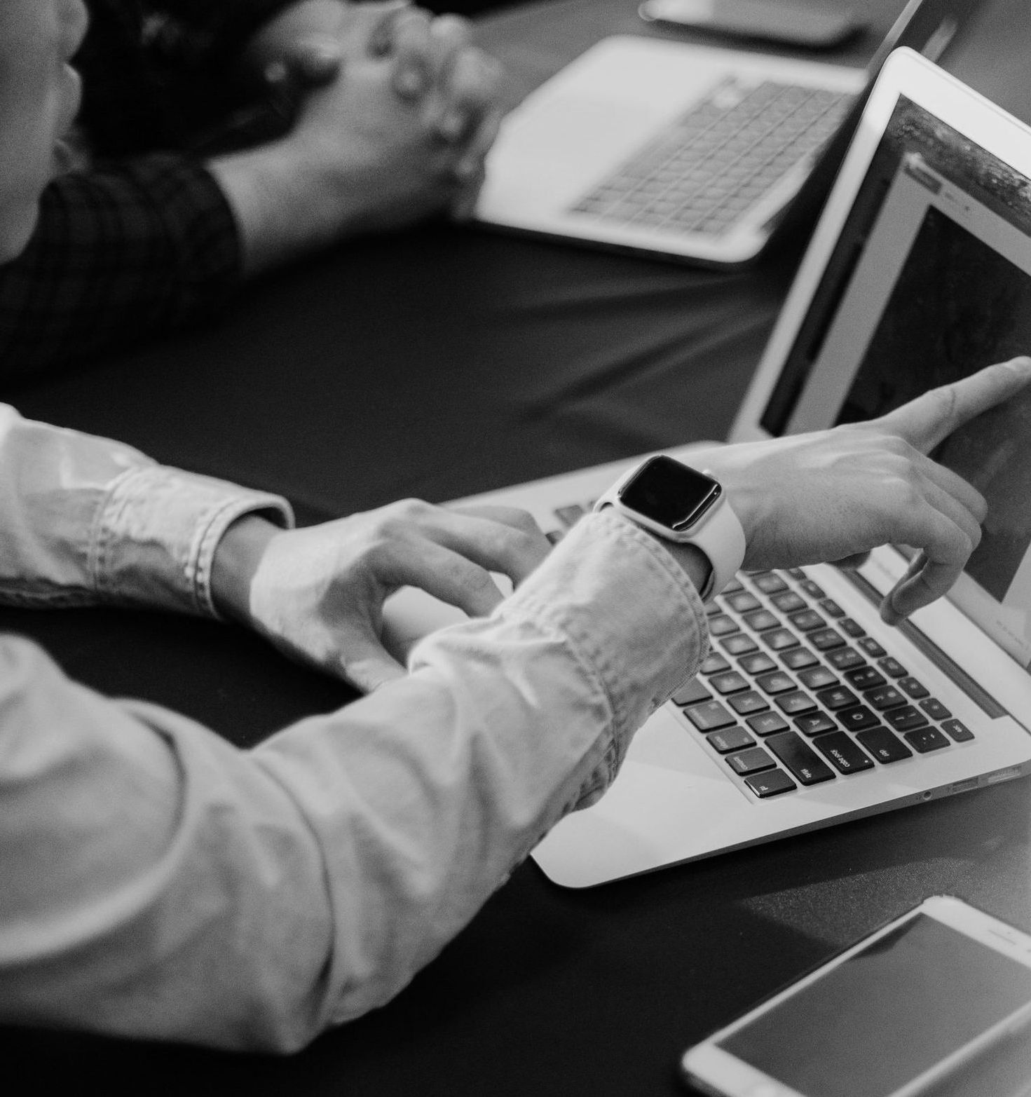 A man wearing an apple watch is typing on a laptop