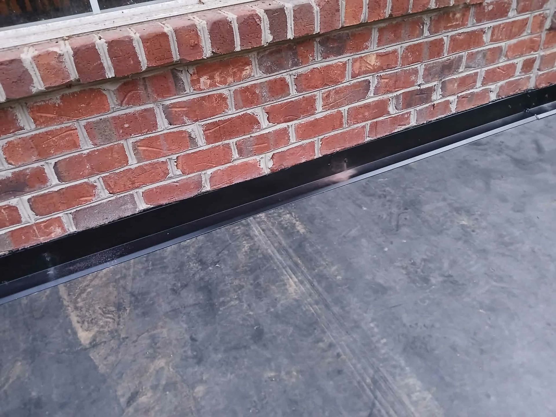 Black roofing material against a brick wall, with a small gap in between.