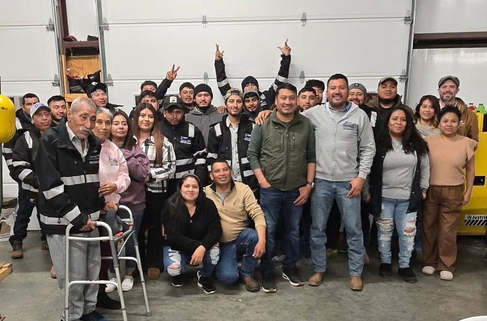 Group of people pose inside a garage. Some stand, others kneel. A few raise hands.