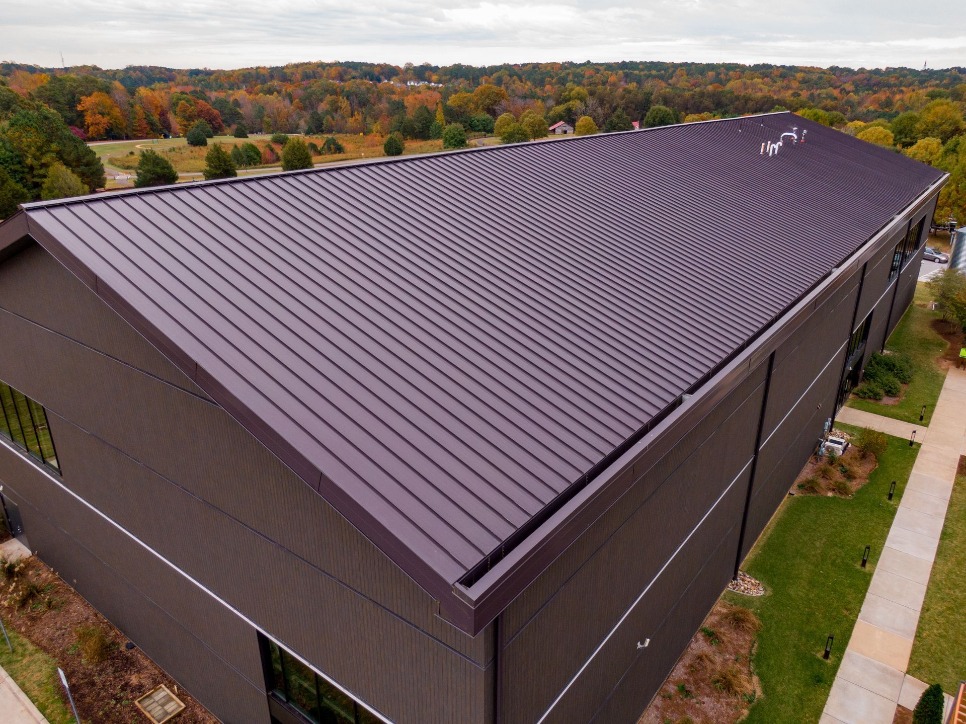 Brown metal roof on a modern building with surrounding autumn trees.
