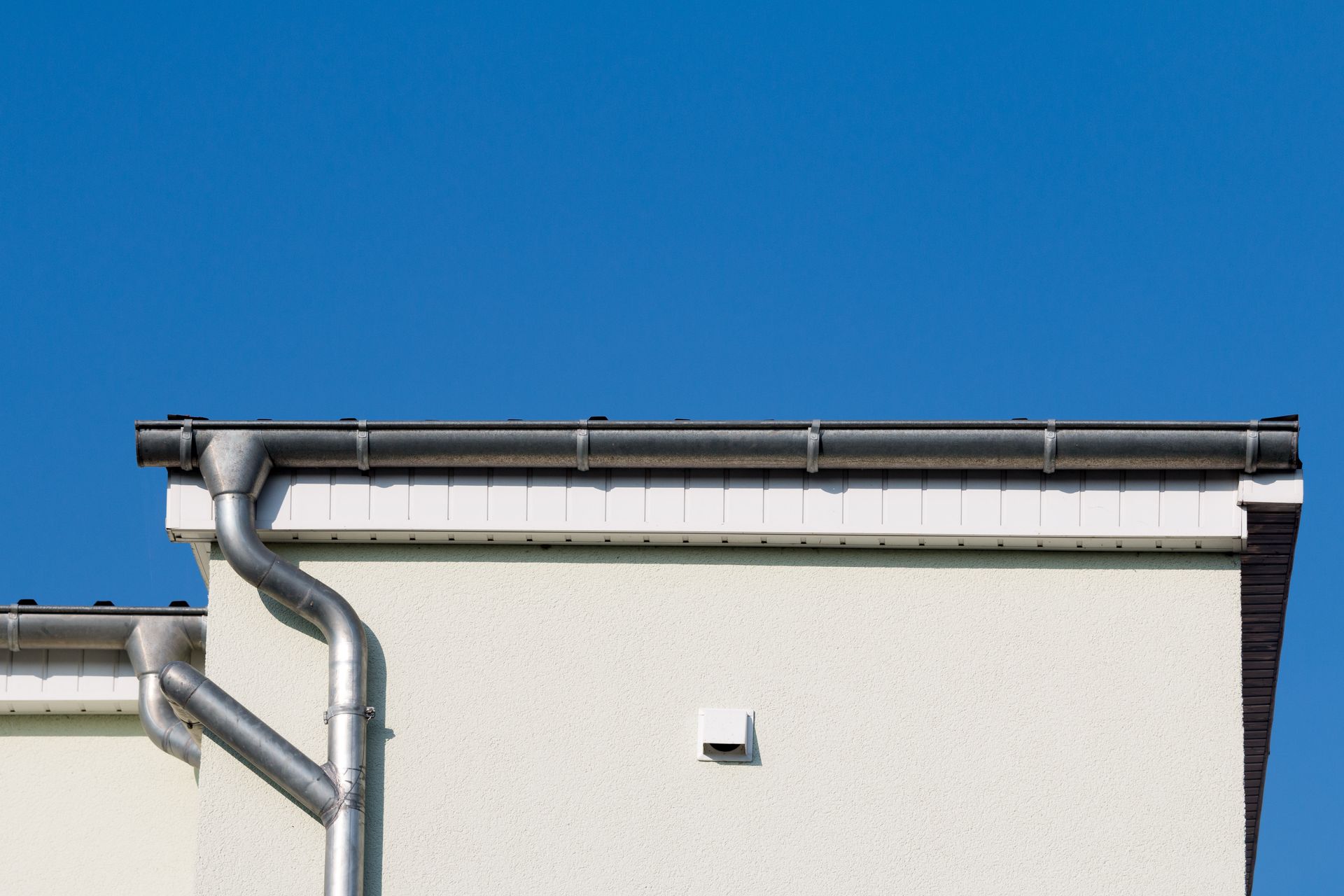 White building with gray gutters and downspouts against a blue sky.